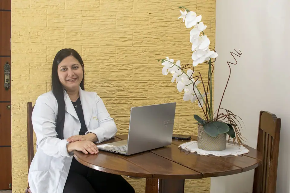 Jeanice Carneiro, da Ergoativa, em sua mesa de trabalho com notebook e um arranjo de orquídeas brancas